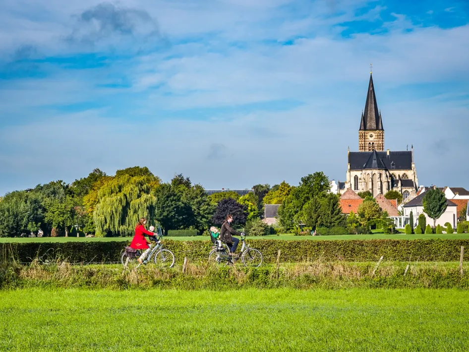 Fietsers in het landschap bij Thorn met uitzicht op de kerk en groene velden tijdens de Puzzelproeverij Maasvallei