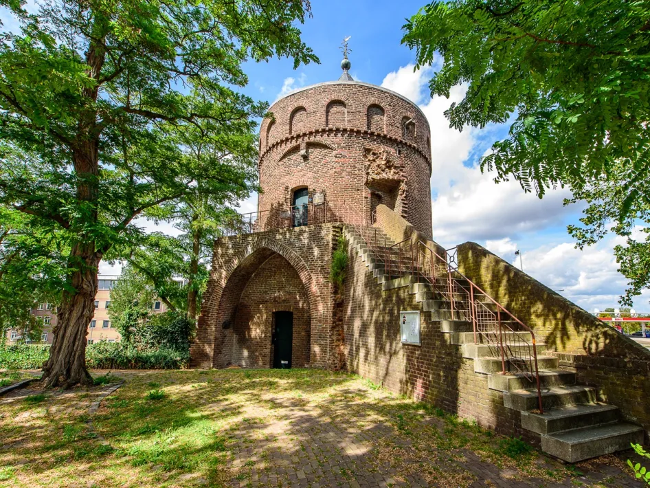 The Rattentoren in Roermond is a medieval defensive tower made of red brick with a stepped gable, surrounded by greenery and a bright blue sky.