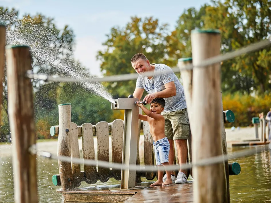 Grote buitenspeeltuin bij Recreatiepark de Leistert met klimrekken, glijbanen en spelende kinderen in het zand.
