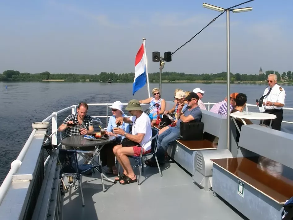 Group of people enjoy a boat ride on the upper deck of a ship flying the Dutch flag, sailing the Maasplassen.