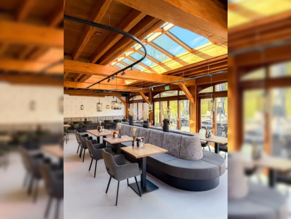 Sitzbereich im Restaurant Aan de Hoeve mit langen Bänken, Tischen und Tageslicht durch das Dachfenster.