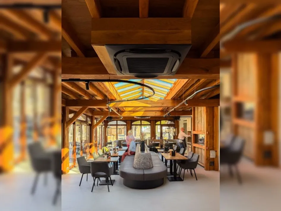 The bright interior of Restaurant Aan de Hoeve with wooden beams, spacious seating and large windows.