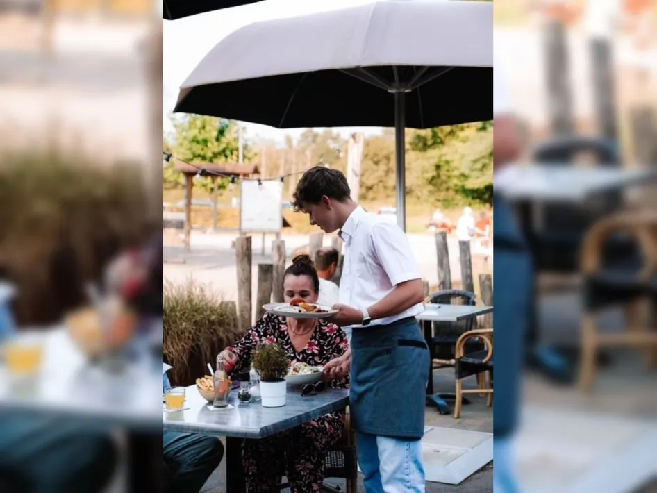 Restaurant Aan de Hoeve met bediening op het terras, waar gasten eten onder een grote parasol.