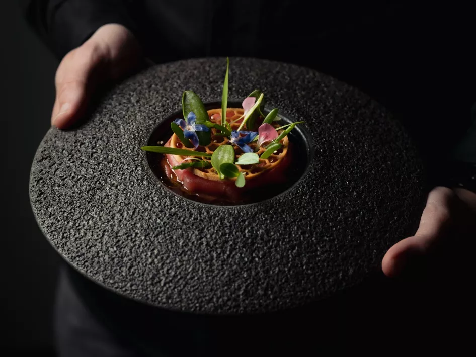Ein eleganter Korridor im Restaurant Damianz mit einem auffälligen, farbenfrohen Kunstwerk an der Wand, moderner Architektur mit Bögen und einem Blick in die Küche. Der Eingang zum Restaurant ist im Hintergrund zu sehen.