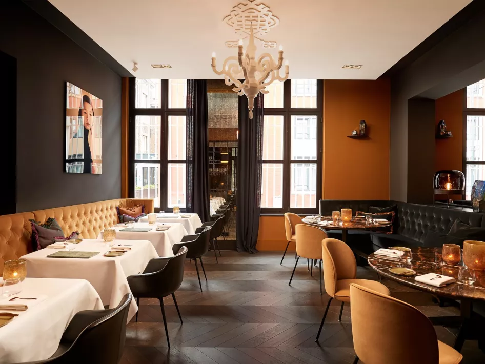 Ein geschmackvoll eingerichteter Essbereich im Restaurant Damianz im Arresthuis, mit elegant gedeckten Tischen, bequemen Stühlen, warmen Farben und großen Fenstern, die viel natürliches Licht hereinlassen.