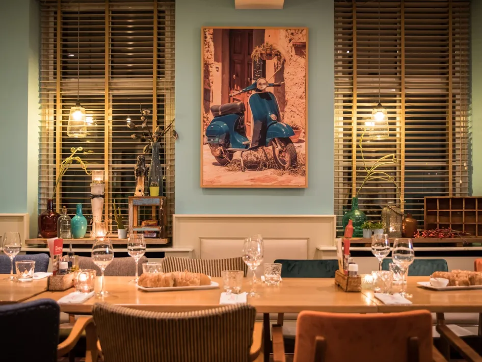 Set tables with glasses and bread in a colourful interior with a Vespa painting on the wall.