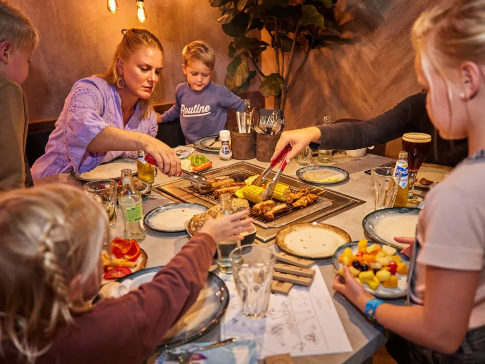 Familie grillt gemeinsam Fleisch und Gemüse am Tisch im Restaurant Grillo im De Leistert.