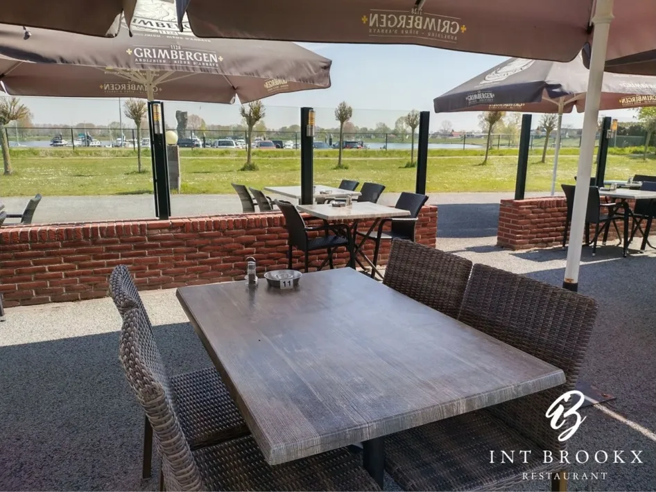 Zonnig terras met houten tafels en uitzicht op het water.