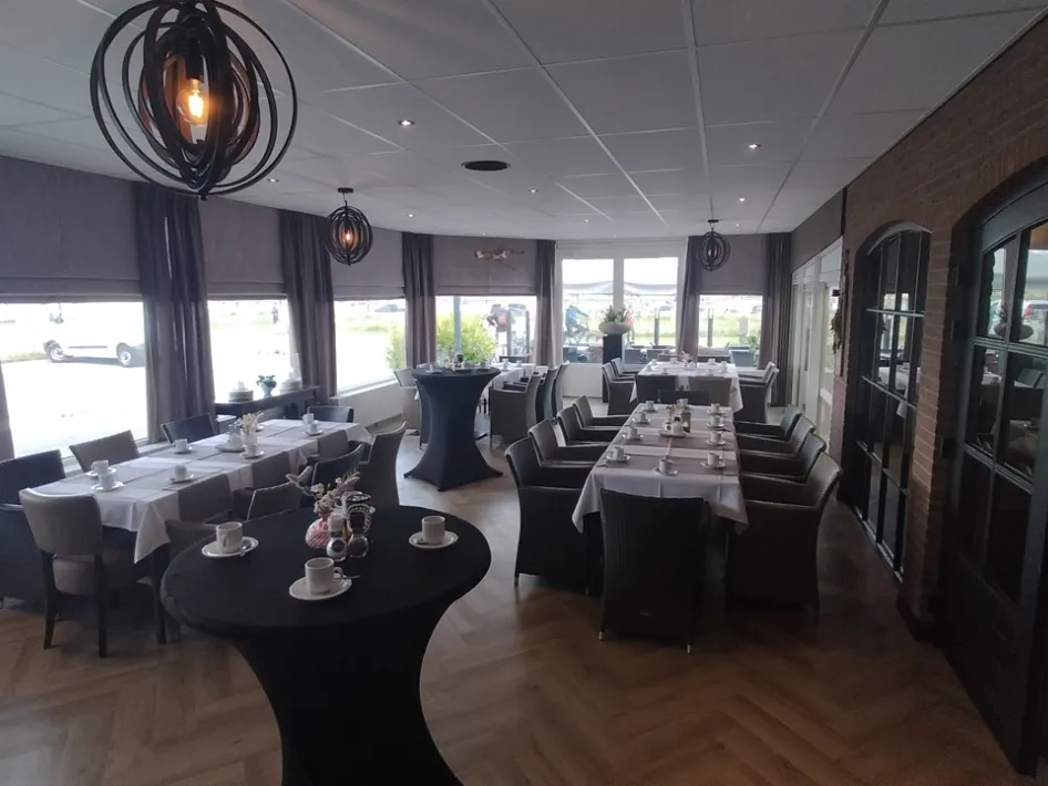 Sfeervolle eetzaal met gedekte tafels, donkere stoelen en moderne verlichting.