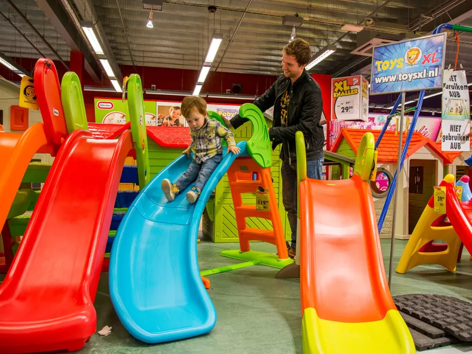 Sohn rutscht eine Rutsche hinunter, während der Vater im Spielwarengeschäft im Retail Park zusieht