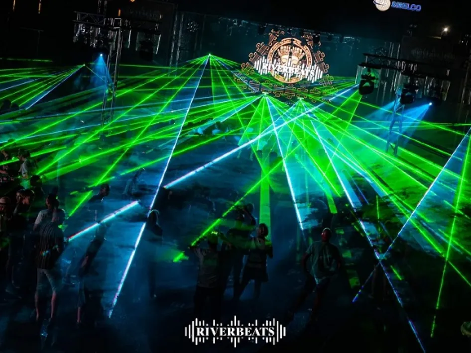 Evening shot of RiverBeats Festival with green and blue lasers above the dancing crowd in Wessem.