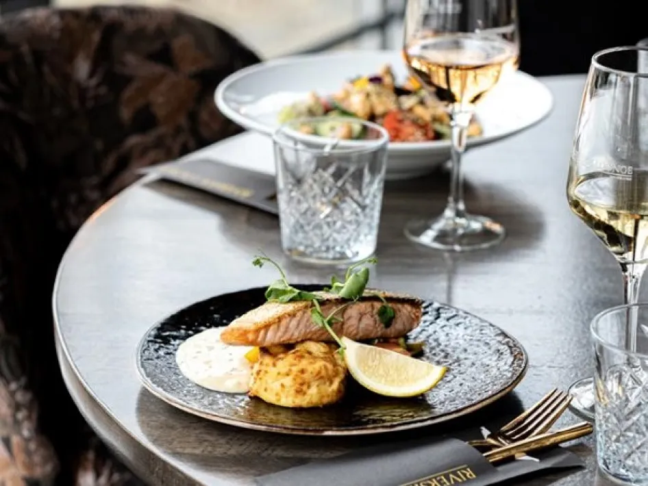Serviertes Gericht mit Lachs, Wein und Wasser auf dem Tisch in der Riverside Lounge