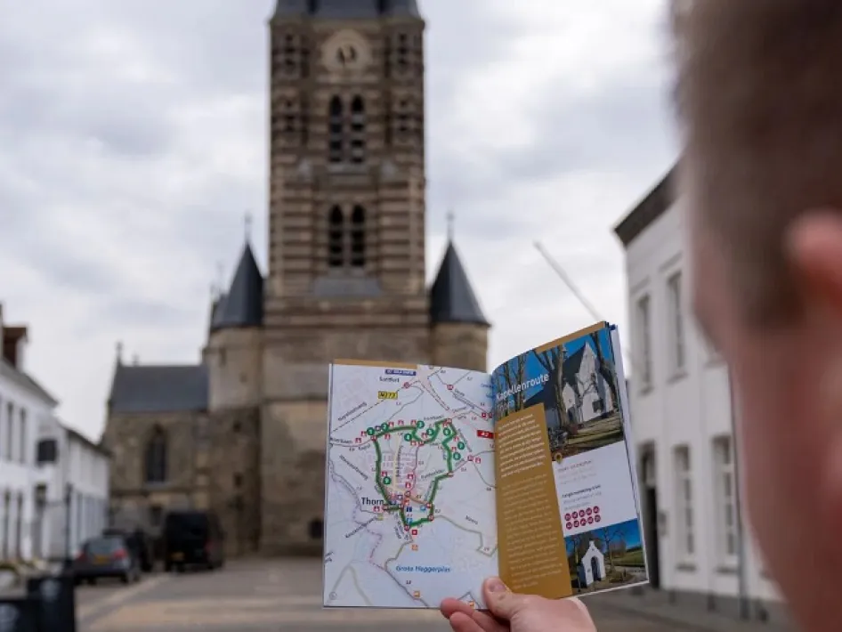 Persoon houdt wandelroutekaart omhoog in Thorn, met de kerk op de achtergrond