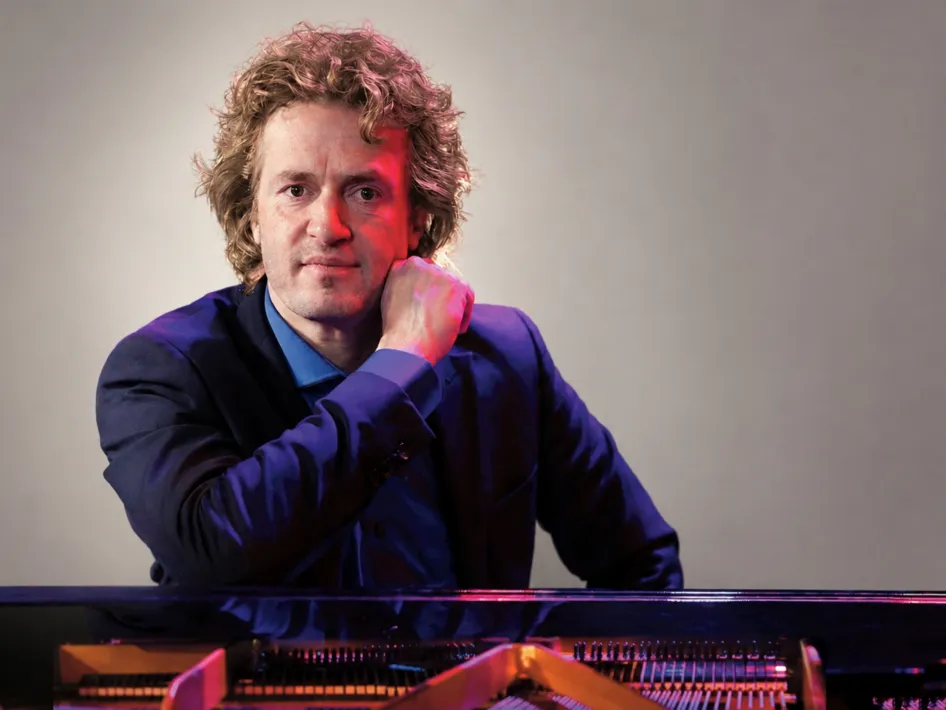 Roon Staal, pianist tijdens het herfstconcert in Stevensweert, achter de piano tijdens een portretfoto met rood en blauw licht.
