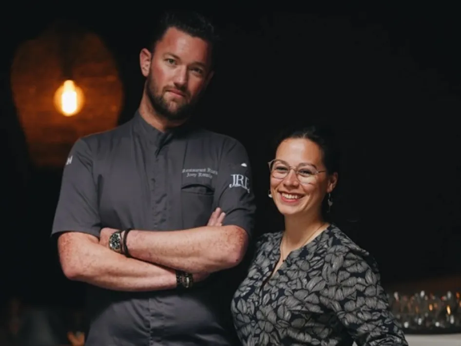 Küchenchef Joey und Gastgeberin Naomi posieren im Restaurant, mit warmem Licht im Hintergrund.