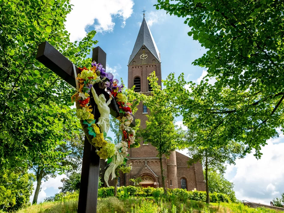 Mit einem bunten Blumenkranz geschmückte Christusstatue vor der Sint Martinus Kirche in Linne