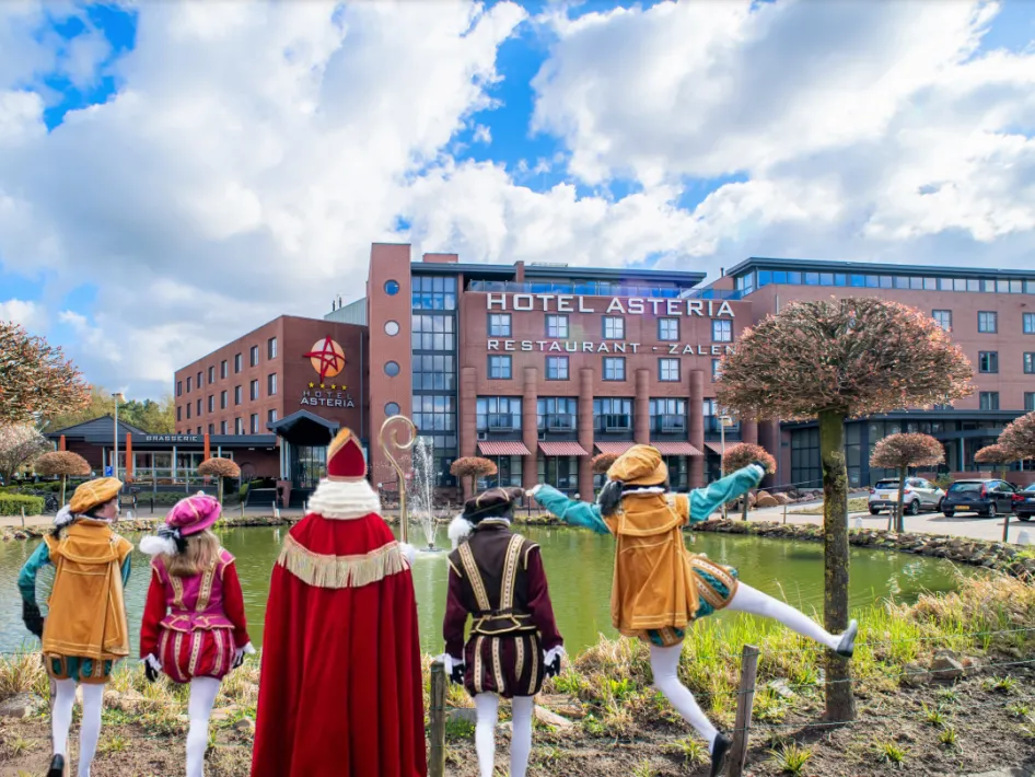 Sinterklaas en vier Pieten bij de vijver voor Hotel Asteria Venray, met op de achtergrond het hotelgebouw onder een blauwe lucht met wolken waar de Sinterklaasbrunch plaatsvindt.