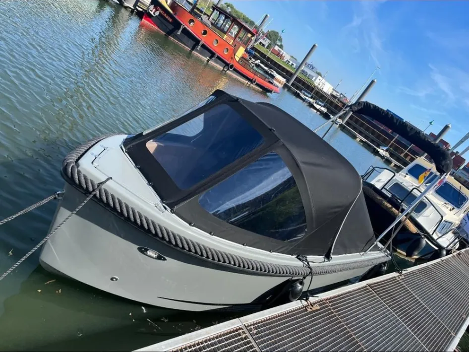Eine vertäute Schaluppe mit schwarzem Verdeck liegt im Hafen, umgeben von anderen Booten und unter einem strahlend blauen Himmel.