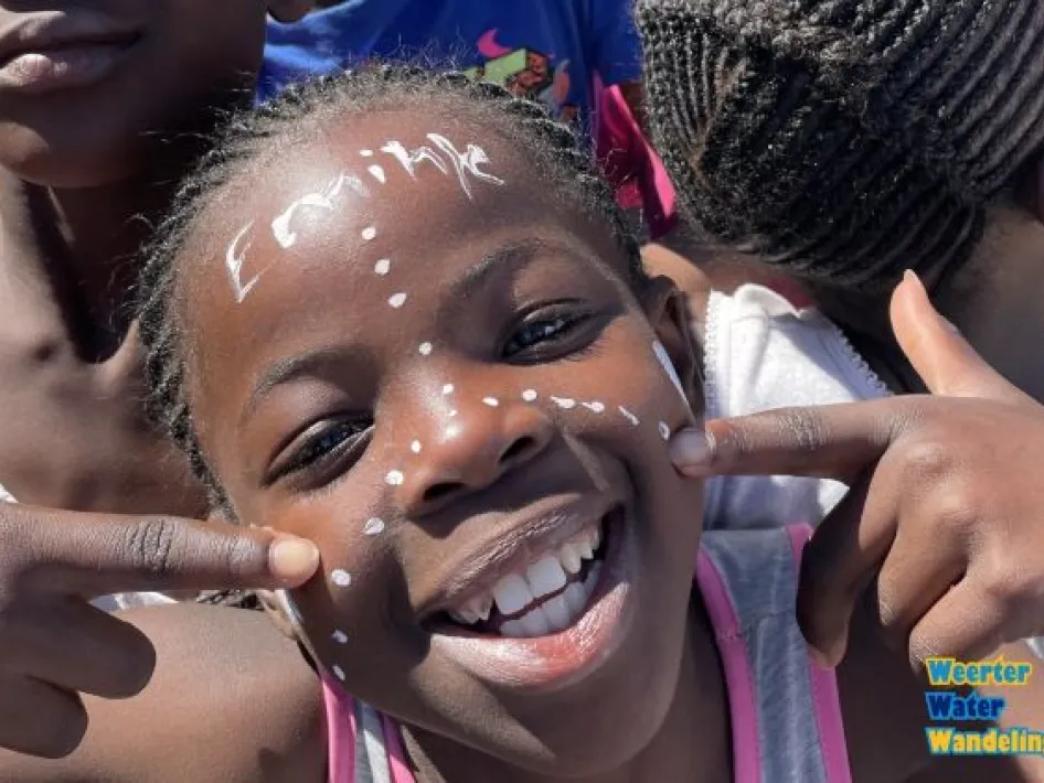 Lachend kind met witte gezichtsschmink wijst naar stippen op haar wangen tijdens de Weerter Waterwandeling.