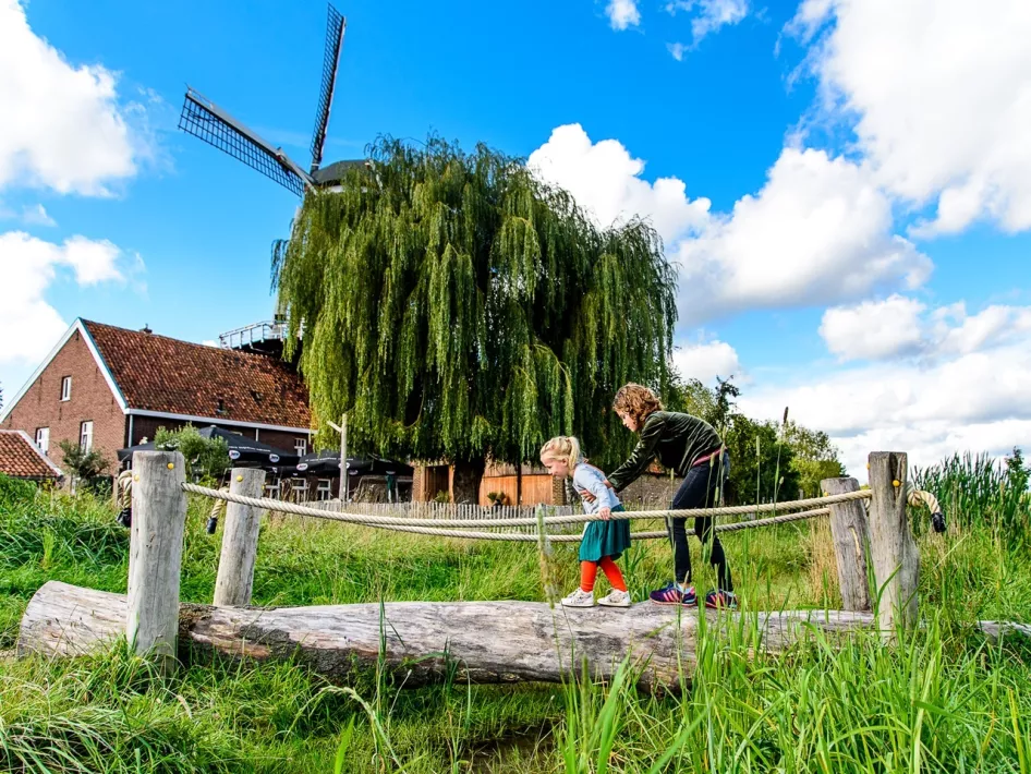 Meisje begeleidt haar zusje over een boomstam in de speeltuin