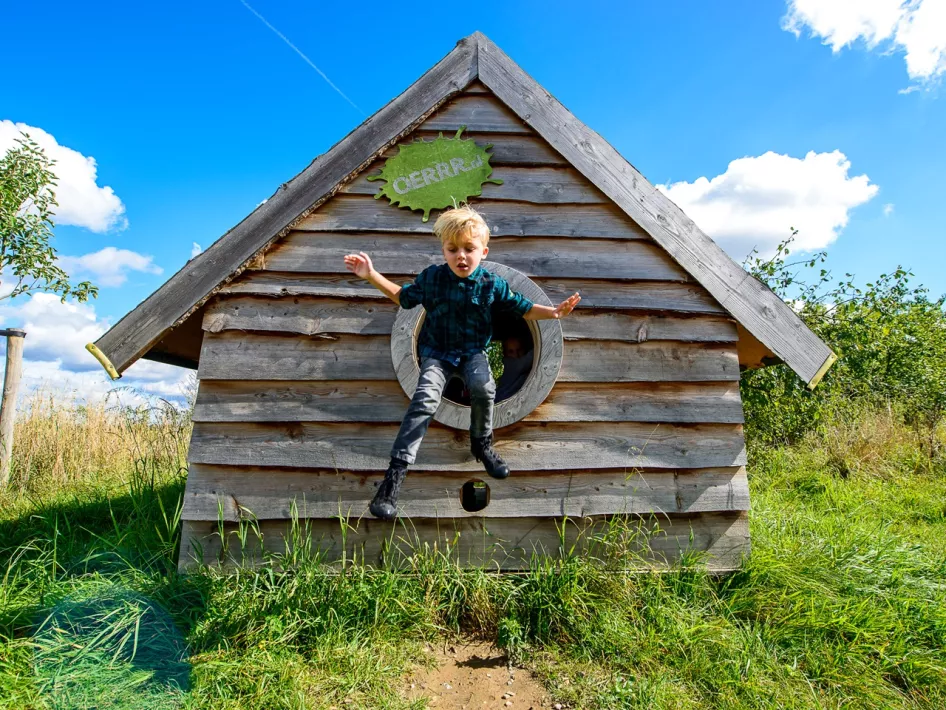 Jongen springt uit een houten speelhuisje bij Speelnatuur OERRR