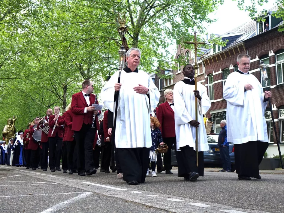 Priesters, gekleed in het wit, leiden de processie met vlak daarachter de Koninklijke Harmonie van Roermond