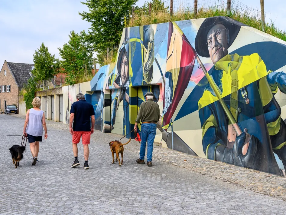 Walkers with dogs passing a colourful mural in Stevensweert