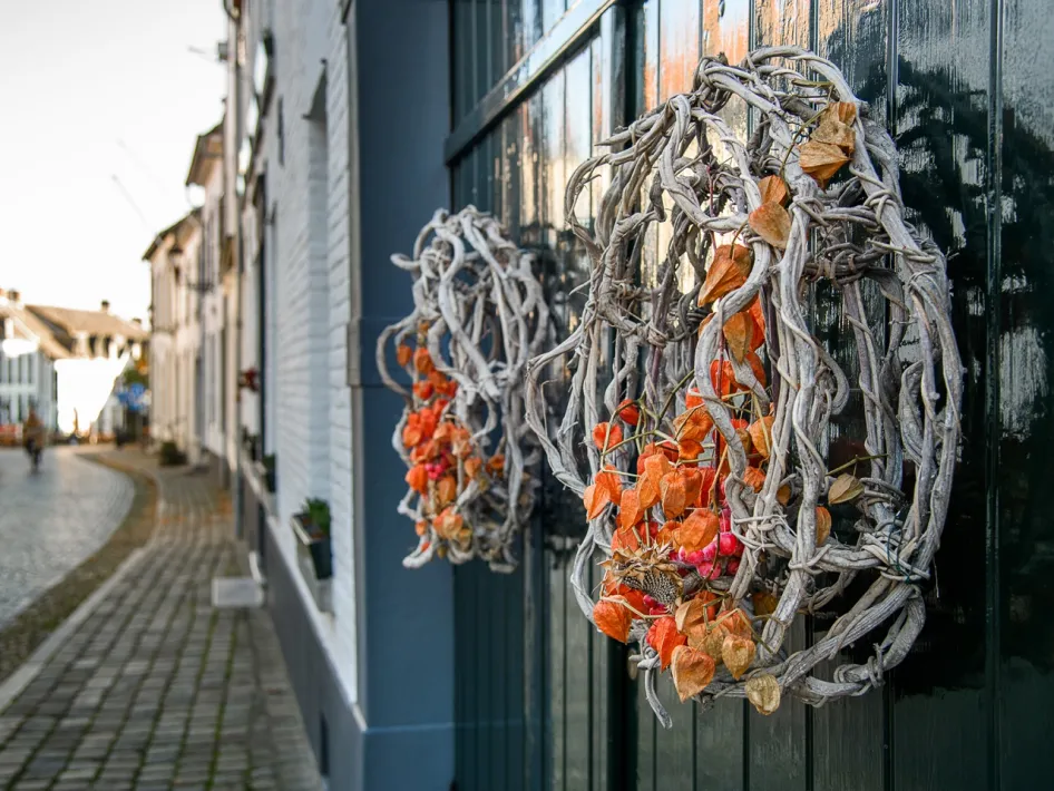 Herfstkransen met oranje en bruine tinten aan een deur in het witte stadje Thorn