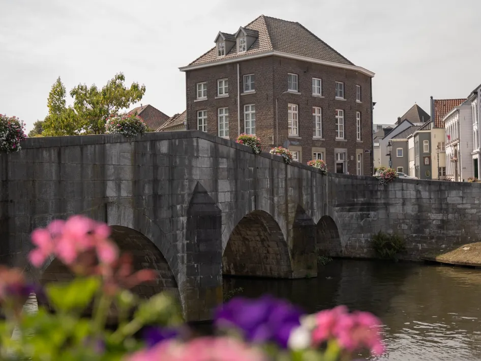 Historische Steenen Brug over de Roer, omringd door monumentale gebouwen en bloemen in de binnenstad van Roermond.
