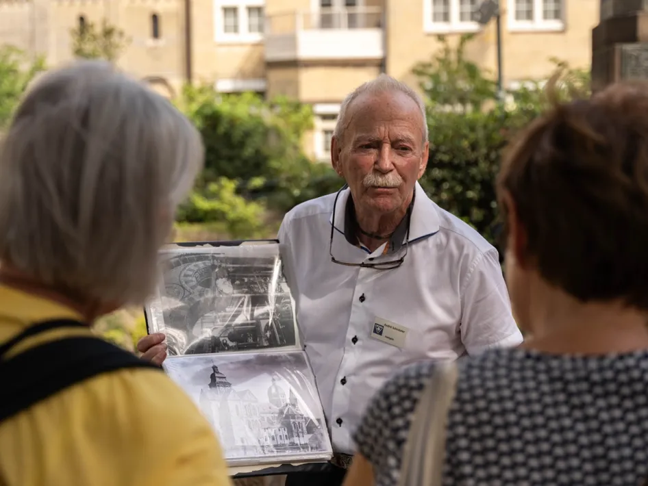 VVV-gids vertelt tijdens een stadswandeling Roermond verhalen aan een groep en toont historische foto’s van de stad.