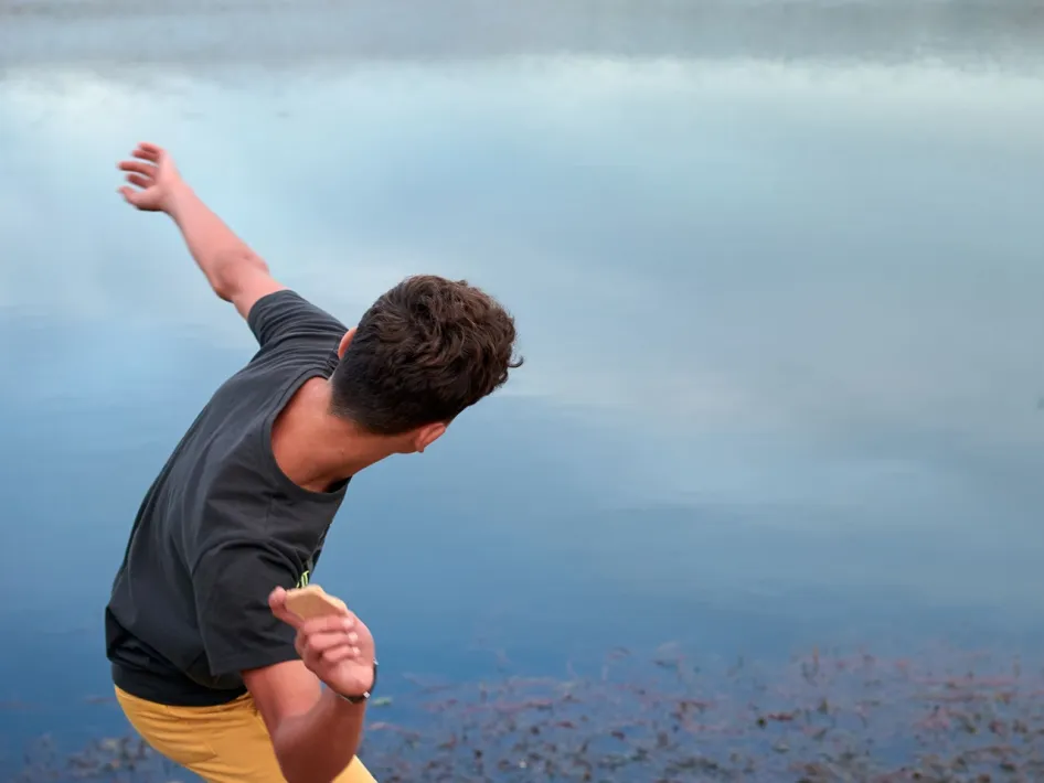 Jongen gooit een platte steen over het water tijdens stone skimming aan een rustige plas.
