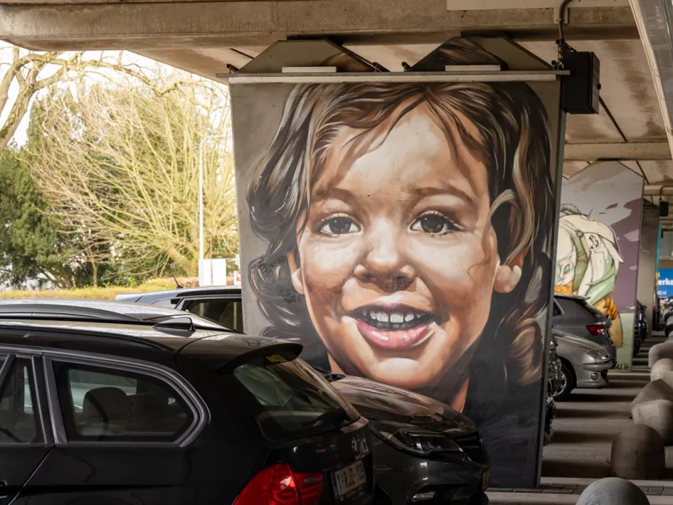 Street art van een lachend kind, geschilderd op een betonnen pilaar in een parkeergarage in Weert. Dit kunstwerk is onderdeel van de Street Art Wandeling Weert.