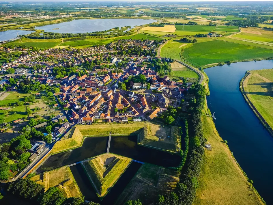 Luchtfoto van vestingstad Stevensweert met zicht op het Eiland in de Maas, omringd door water, groene velden en de Maasplassen in de verte.
