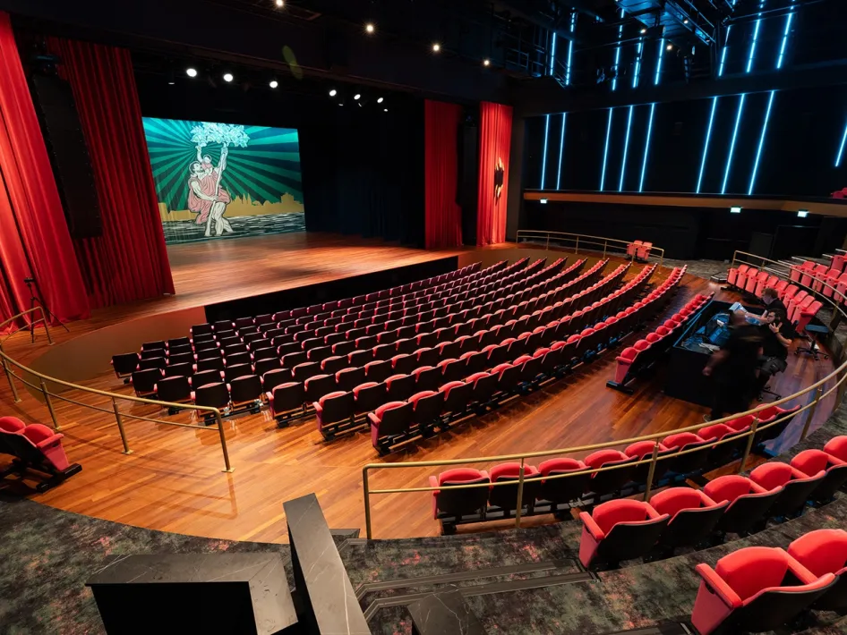 Grote theaterzaal met rode stoelen en ruim podium, klaar voor een voorstelling.