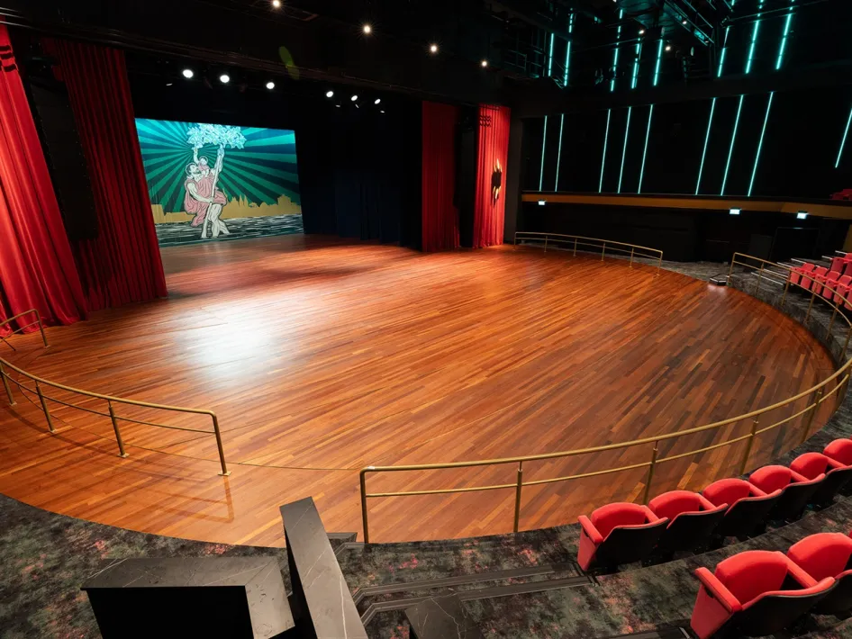 Groot leeg podium in Theater De Oranjerie met houten vloer en rode theatergordijnen aan weerszijden.