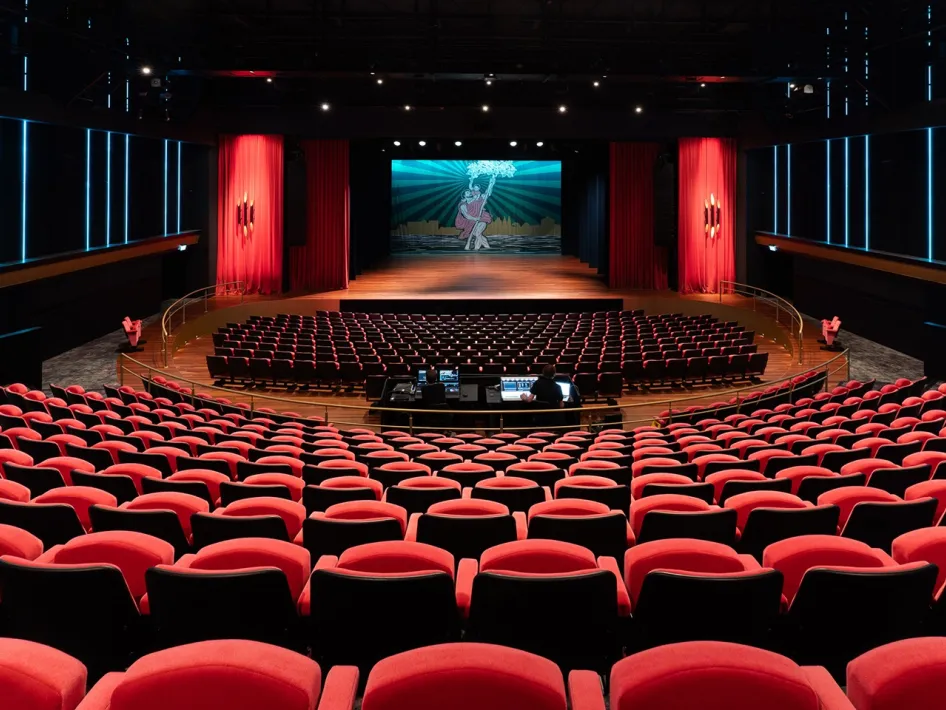 Uitzicht vanaf de achterste rijen van de theaterzaal van Theater De Oranjerie op het podium met rode stoelen op de voorgrond.