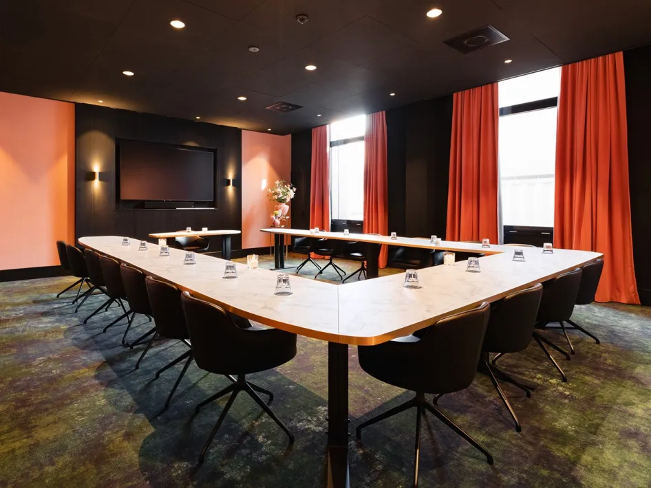 Vergaderzaal van TheaterHotel De Oranjerie in Roermond met U-opstelling, scherm en moderne inrichting.