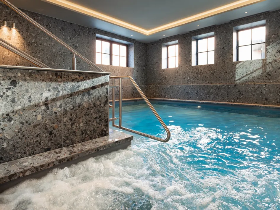 Innenpool mit klarem, blauem Wasser, Whirlpool im Vordergrund und Treppe mit Edelstahlgeländer.