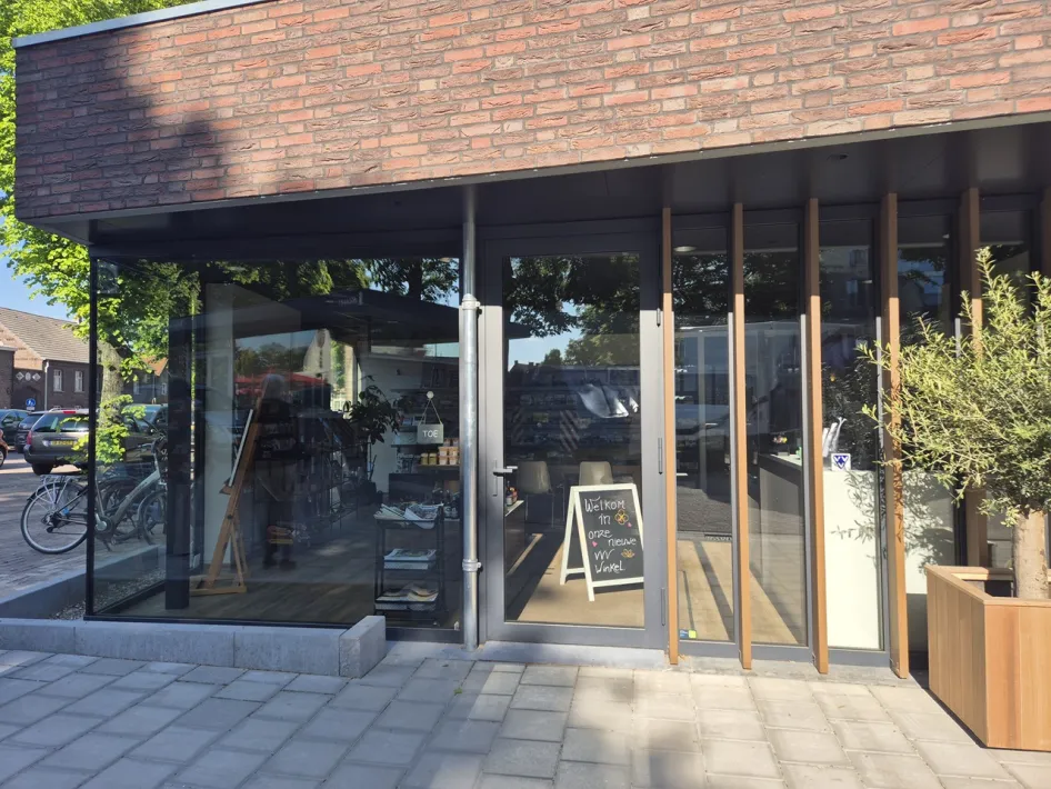 Vooraanzicht van de nieuwe VVV in Kessel met glazen gevel, houten details en een stoepbord bij de ingang.