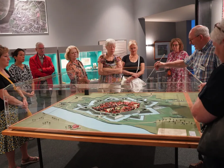 Groep bezoekers luistert naar een gids die uitleg geeft bij een maquette van de vesting Stevensweert in een museum.