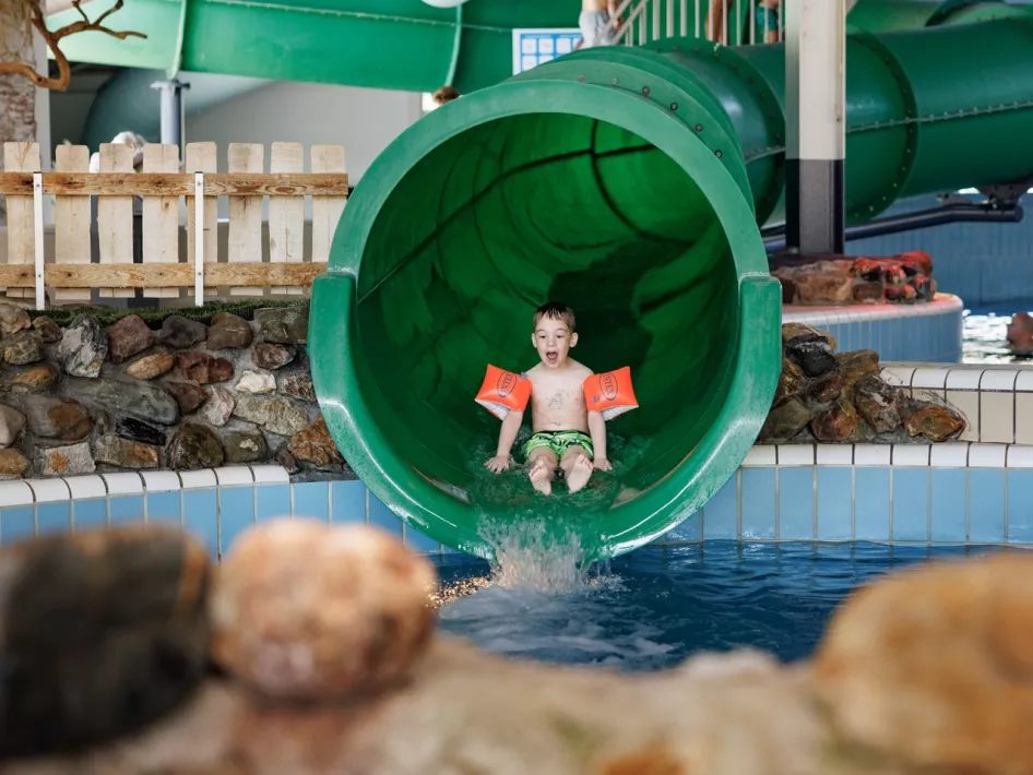 Kind rutscht die Rutsche im subtropischen Schwimmbad von Roompot Weerterbergen hinunter