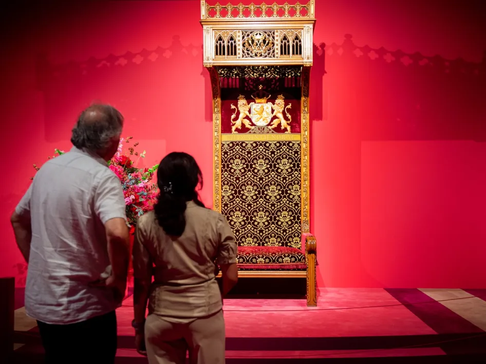 Twee bezoekers bekijken de rijkversierde troon tijdens de expositie Van Maker tot Majesteit in het Cuypershuis in Roermond.