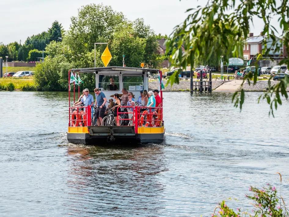Veerpont met fietsers en voetgangers steekt de Maas over tussen Neer en Beesel op een zomerse dag.