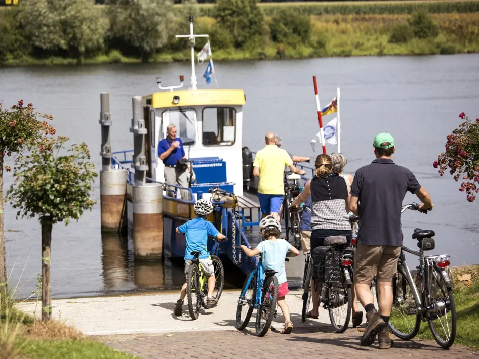 Eine Familie mit Fahrrädern besteigt die Fuß- und Fahrradfähre Blitterswijck-Wellerlooi, um an einem sonnigen Tag die Maas zu überqueren.