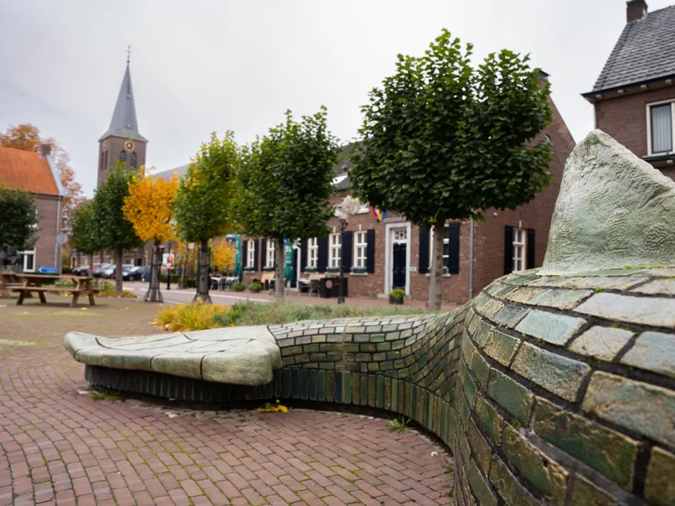 The artwork ‘Dragon's Tail’ on the Market Square in Beesel, with the church and cosy terraces in the background.