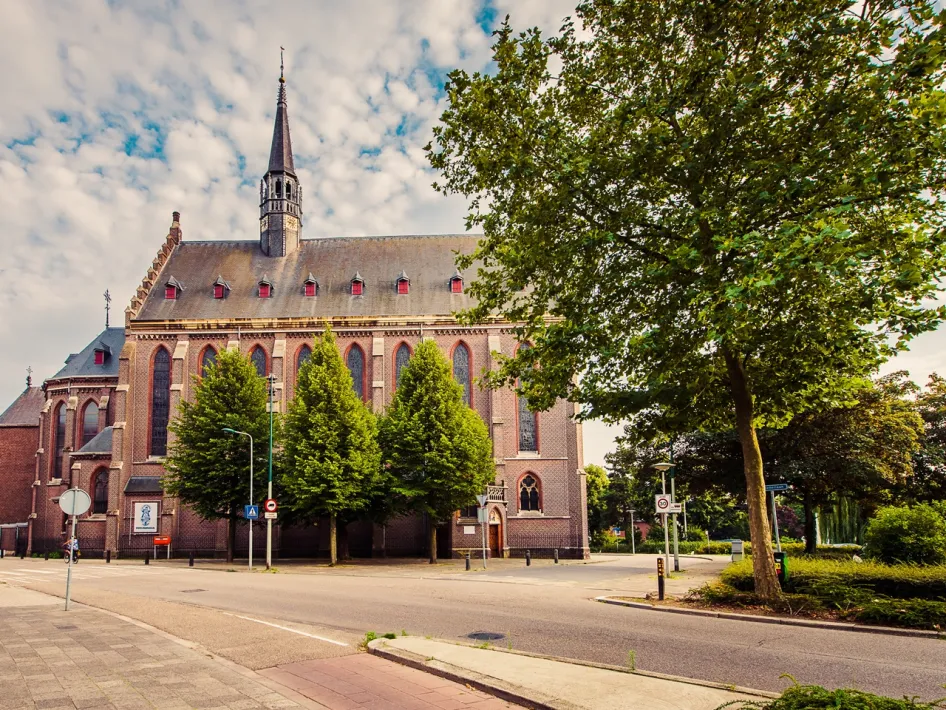 Brick church, the Kapel in 't Zand, with a high spire and trees along the road on the City walking route - Het Kapeller Kwartier in Roermond.