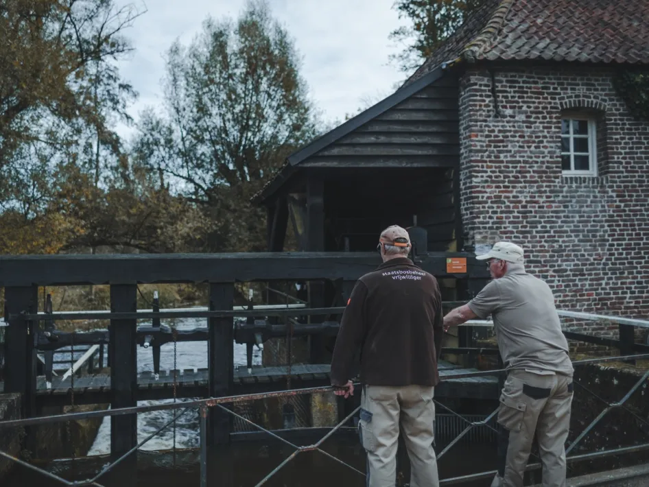 Zwei Freiwillige am Wasserrad der Ursulamühle in grüner Landschaft.