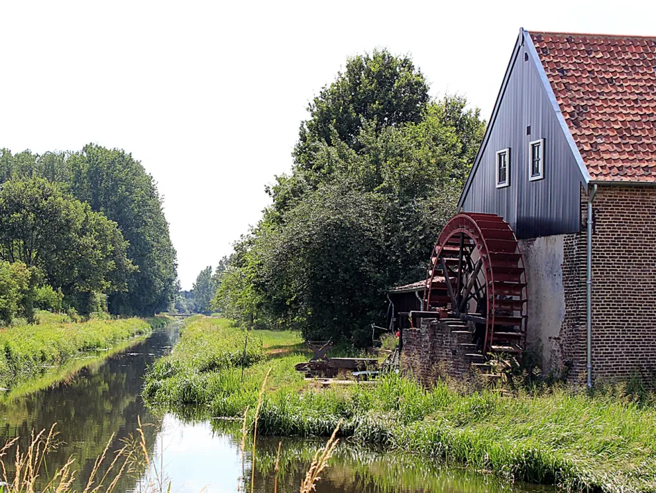 Uffelse Mühle am Wasser mit großem Mühlrad und grünen Ufern, Teil der Wanderroute Neeritter und Uffelse Beek