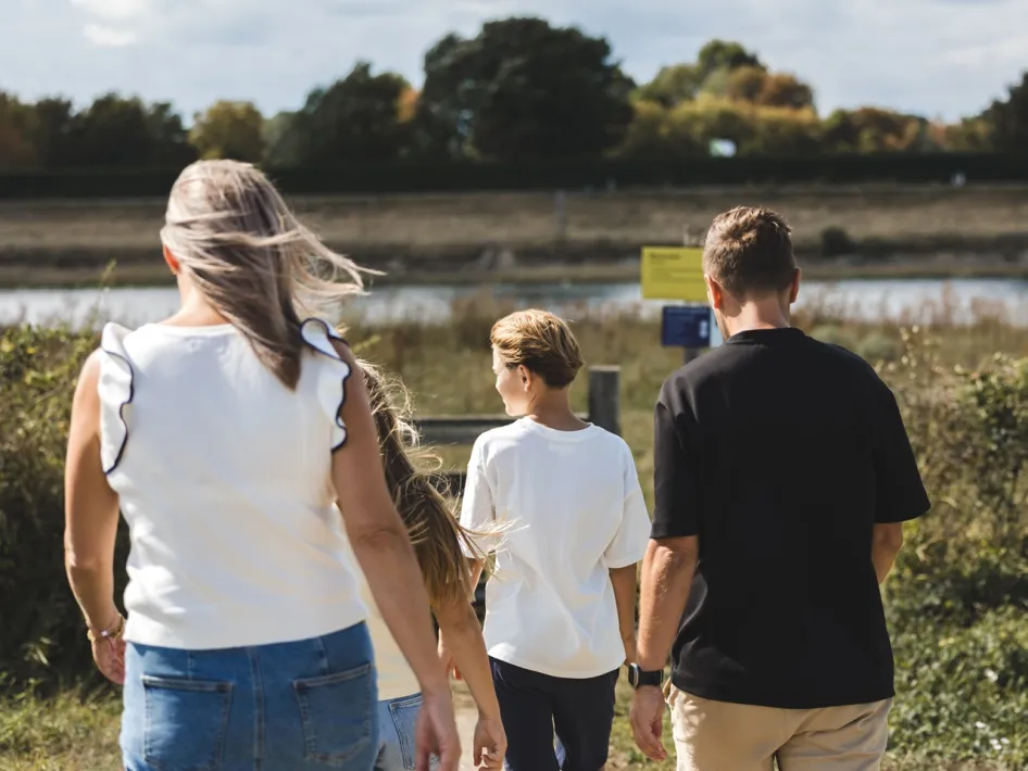 Gezin met twee kinderen wandelt over een smal pad langs het water in Rivierpark Maasvallei.