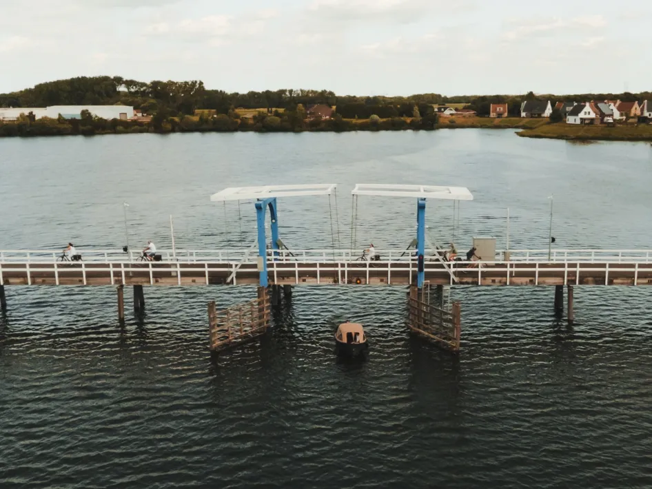 Fietsers op een brug over het water bij Thorn, met een boot onder de brug, in de omgeving van Wandelroute Rivierpark Maasvallei.